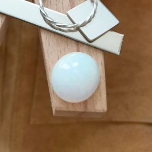 The white opal oval cabochon displayed on a jewellers bench peg with some sterling silver sheet and wire.