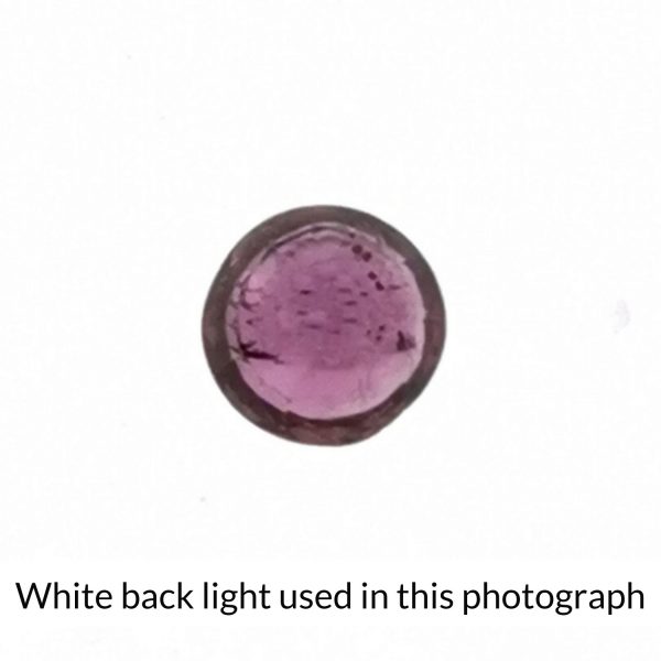 The round shaped ruby gem is being back-lit with a bright white light to show any inclusions within the gem more clearly.