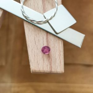 The pinkish red ruby displayed on a jewellers bench peg with some sterling silver sheet and wire.