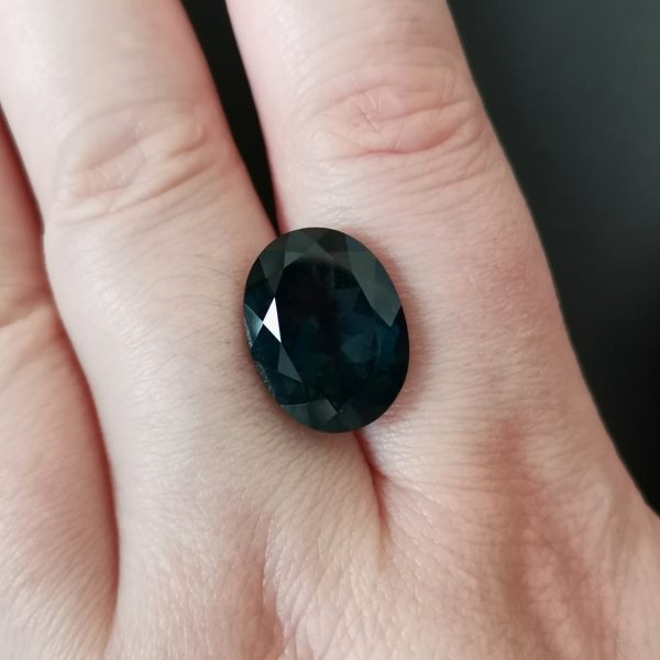 The dark blue topaz gemstone resting on a hand to give an idea of the gemstones size and colour.