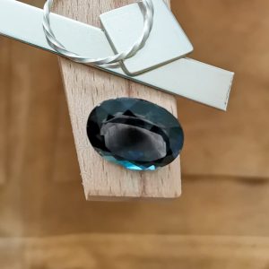 The large dark london blue topaz oval displayed on a jewellers bench peg with some sterling silver sheet and wire.