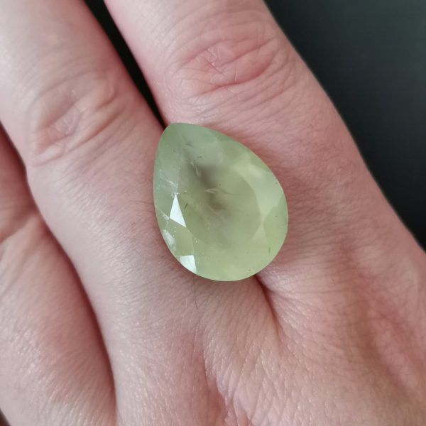 The pale green prehnite gemstone resting on a hand to give an idea of the gemstones size and colour.