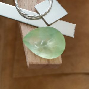 The large green prehnite teardrop displayed on a jewellers bench peg with some sterling silver sheet and wire.