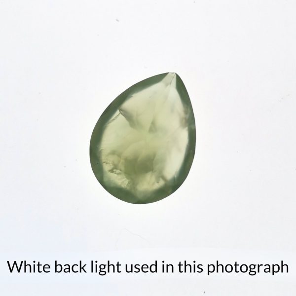 The teardrop shaped prehnite gem is being back-lit with a bright white light to show any inclusions within the gem more clearly.