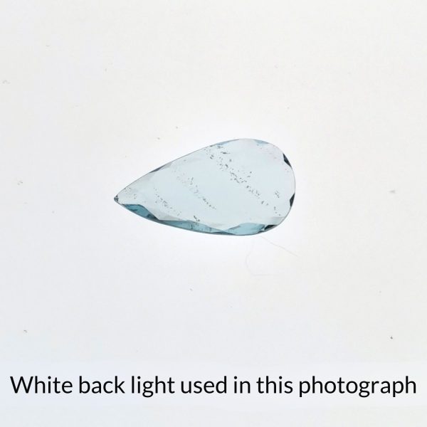 The teardrop shaped aquamarine gem is being back-lit with a bright white light to show any inclusions within the gem more clearly.