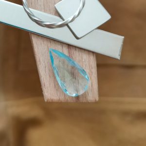 The pale blue aquamarine teardrop displayed on a jewellers bench peg with some sterling silver sheet and wire.