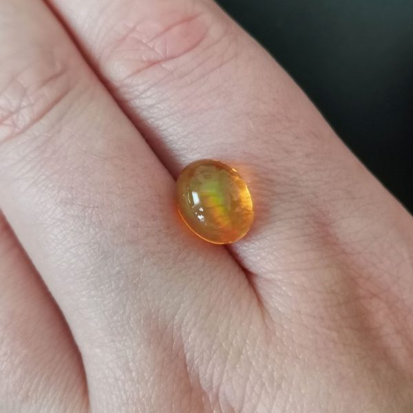 The orange fire opal gemstone resting on a hand to give an idea of the gemstones size and colour.
