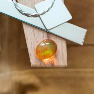 The orange fire opal oval cabochon displayed on a jewellers bench peg with some sterling silver sheet and wire.