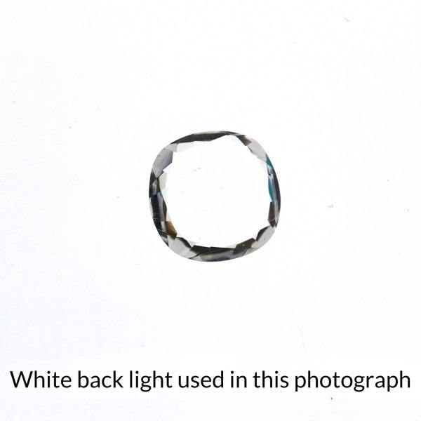 The cushion cut square clear quartz gem is being back-lit with a bright white light to show any inclusions within the gem more clearly.