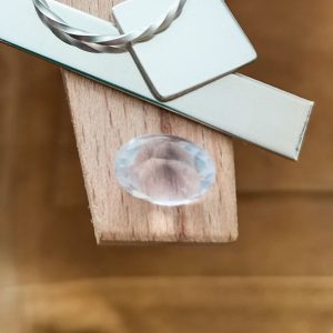 The pale pink oval rose quartz displayed on a jewellers bench peg with some sterling silver sheet and wire.