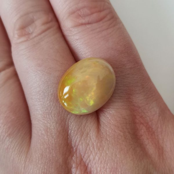 The orange and yellow opal gemstone resting on a hand to give an idea of the gemstones size and colour.