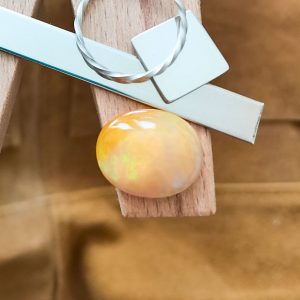 The orange opal oval cabochon displayed on a jewellers bench peg with some sterling silver sheet and wire.