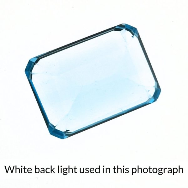 The rectangle shaped topaz gem is being back-lit with a bright white light to show any inclusions within the gem more clearly.