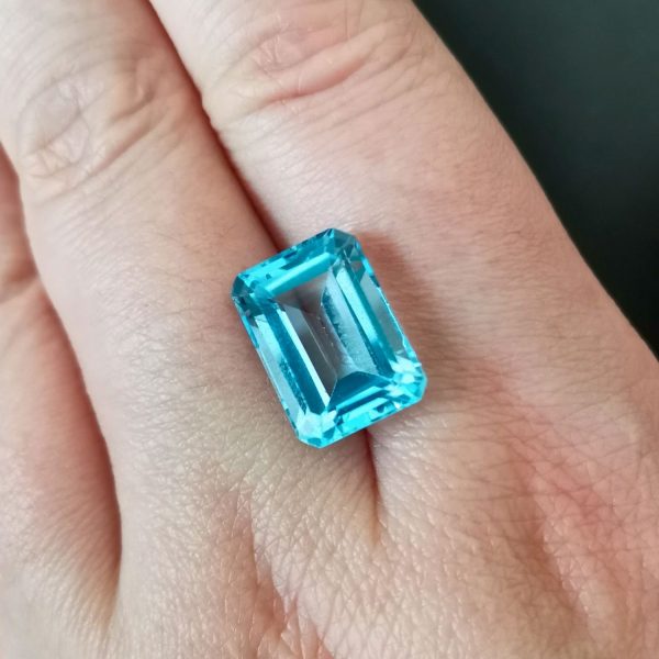 The bright blue topaz gemstone resting on a hand to give an idea of the gemstones size and colour.
