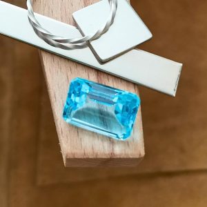 The large bright blue topaz rectangle displayed on a jewellers bench peg with some sterling silver sheet and wire.