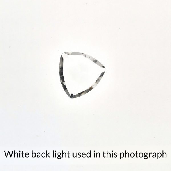 The triangle shaped clear quartz gem is being back-lit with a bright white light to show any inclusions within the gem more clearly.