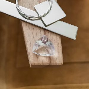The clear quartz triangle displayed on a jewellers bench peg with some sterling silver sheet and wire.