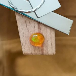 The orange fire opal oval cabochon displayed on a jewellers bench peg with some sterling silver sheet and wire.