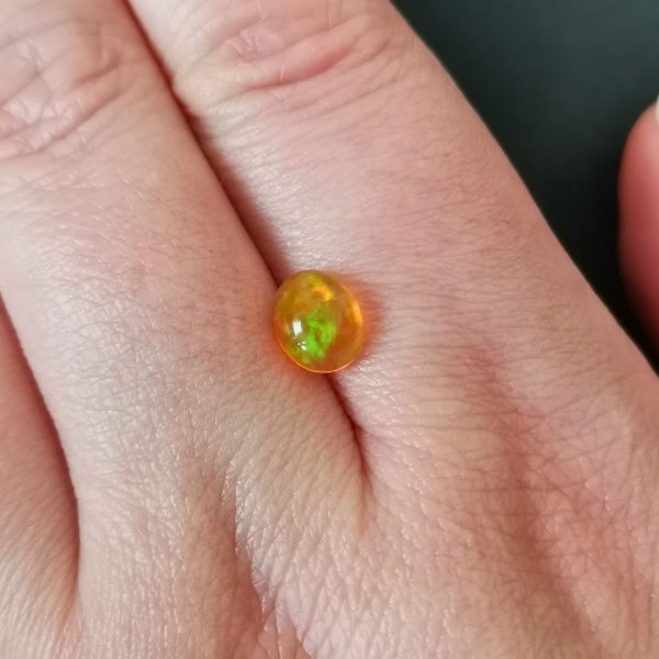 The orange fire opal gemstone resting on a hand to give an idea of the gemstones size and colour.