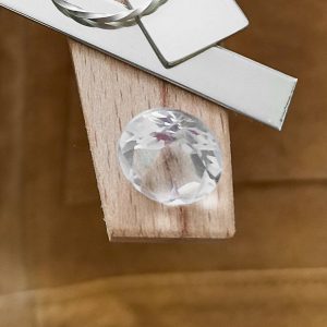 The clear quartz faceted round displayed on a jewellers bench peg with some sterling silver sheet and wire.