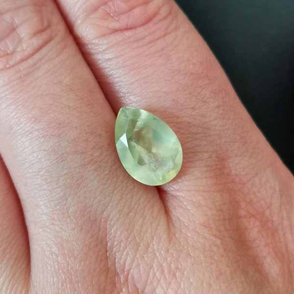 The green prehnite gemstone resting on a hand to give an idea of the gemstones size and colour.