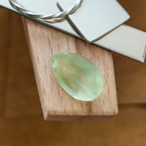 The large pale green prehnite teardrop displayed on a jewellers bench peg with some sterling silver sheet and wire.