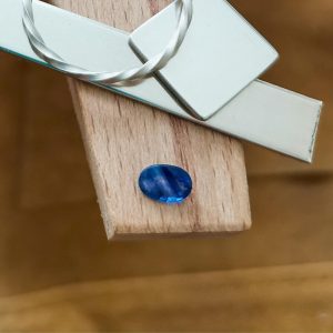 The faceted blue sapphire oval displayed on a jewellers bench peg with some sterling silver sheet and wire.