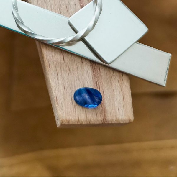 The faceted blue sapphire oval displayed on a jewellers bench peg with some sterling silver sheet and wire.