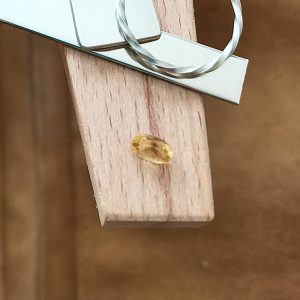 The yellow heliodor oval displayed on a jewellers bench peg with some sterling silver sheet and wire.