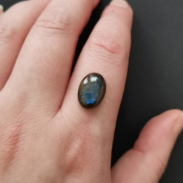 The dark labradorite gemstone resting on a hand to give an idea of the gemstones size and colour.