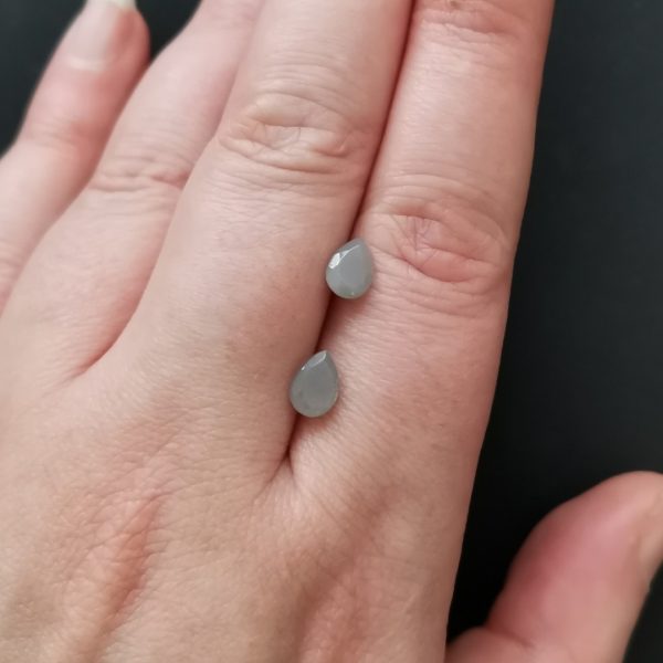 The pair of grey moonstone gemstone resting on a hand to give an idea of the gemstones size and colour.