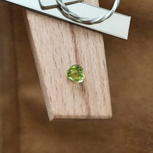 The green peridot heart displayed on a jewellers bench peg with some sterling silver sheet and wire.