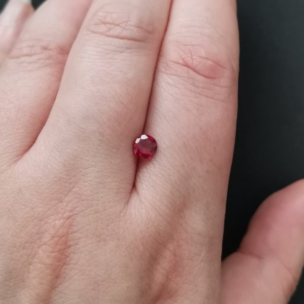 The small red ruby gemstone resting on a hand to give an idea of the gemstones size and colour.