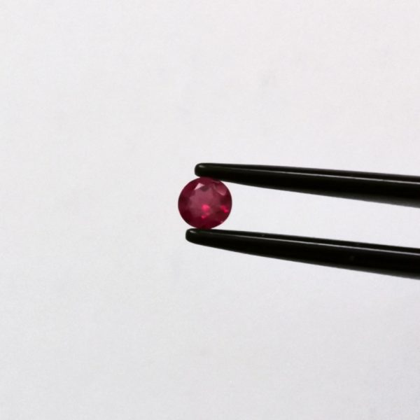 A photo of the crown area of the dark pinkish red ruby against a white background