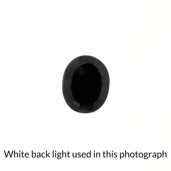 The black sapphire oval gem is being back-lit with a bright white light to show any inclusions within the gem more clearly.