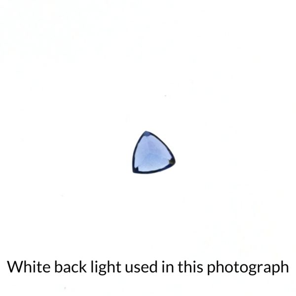 The trillion cut tanzanite gem is being back-lit with a bright white light to show any inclusions within the gem more clearly.
