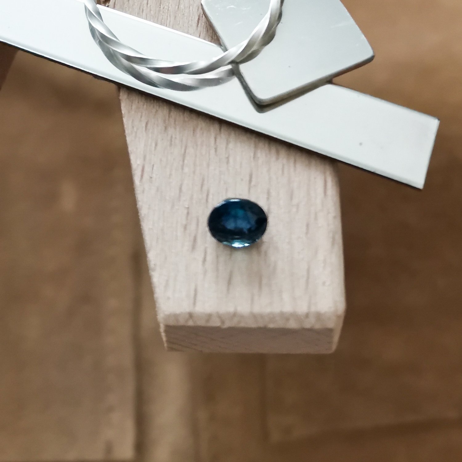 The blue sapphire oval displayed on a jewellers bench peg with some sterling silver sheet and wire.