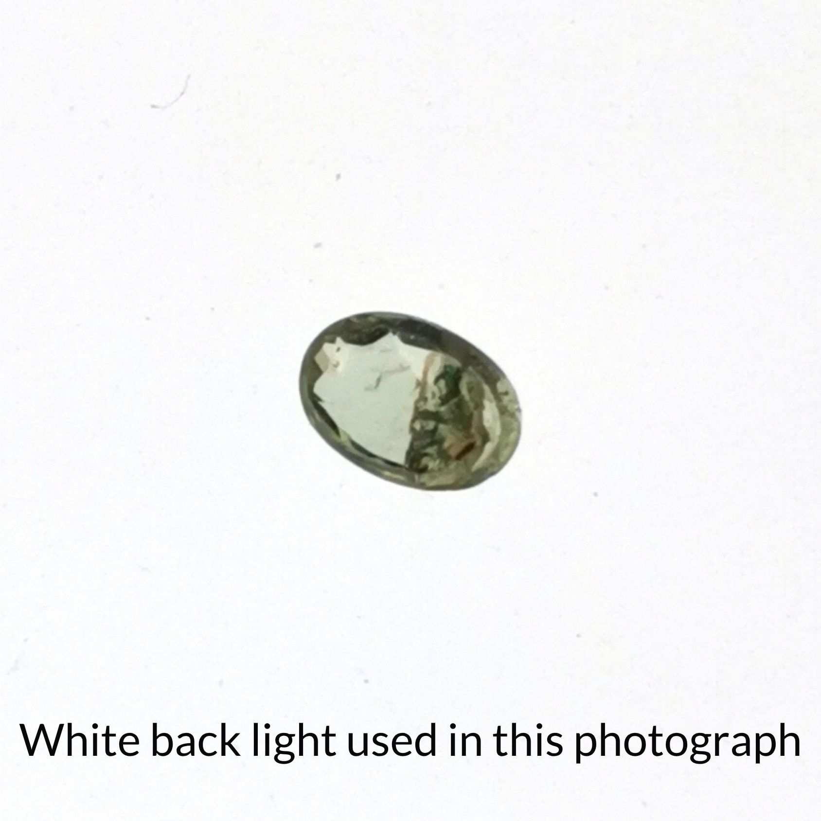 The green sapphire oval gem is being back-lit with a bright white light to show any inclusions within the gem more clearly.