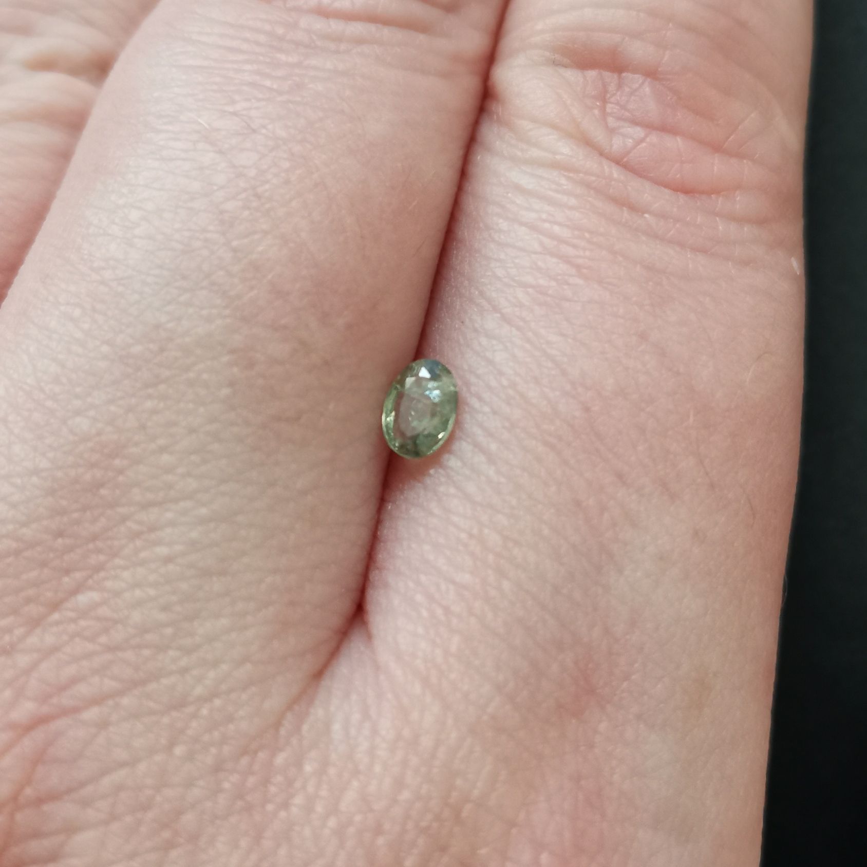 The pale green sapphire gemstone resting on a hand to give an idea of the gemstones size and colour.