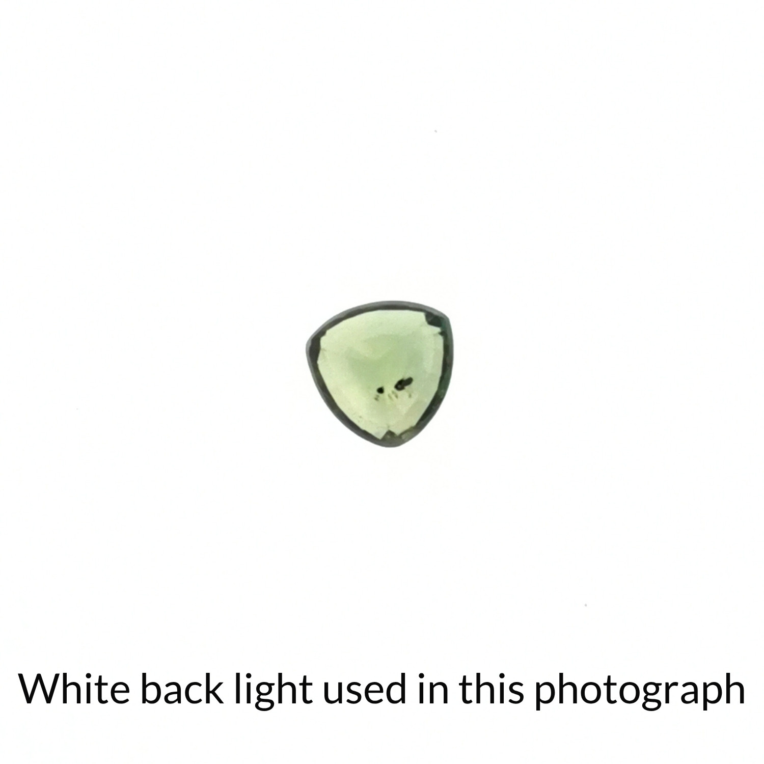 The green sapphire triangle gem is being back-lit with a bright white light to show any inclusions within the gem more clearly.
