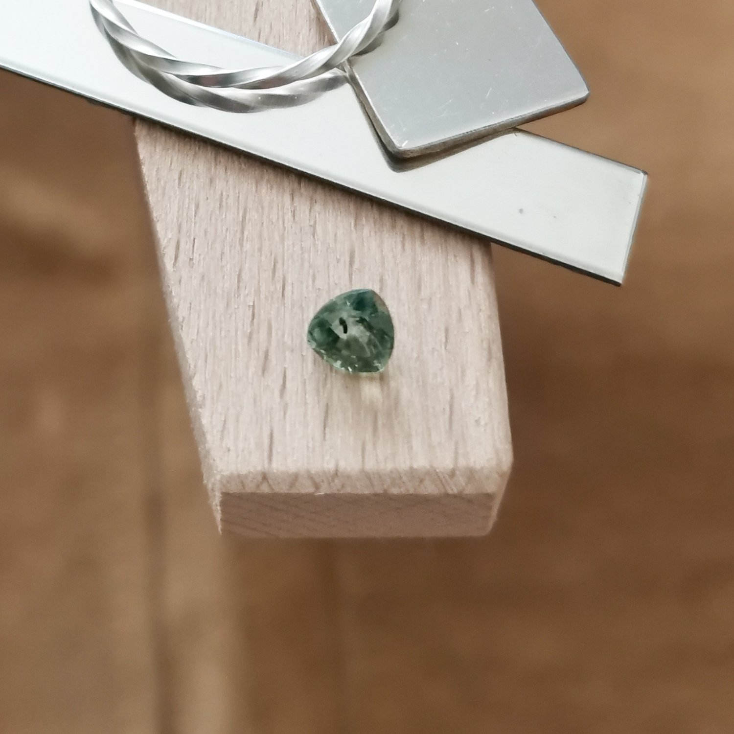 The green sapphire triangle displayed on a jewellers bench peg with some sterling silver sheet and wire.