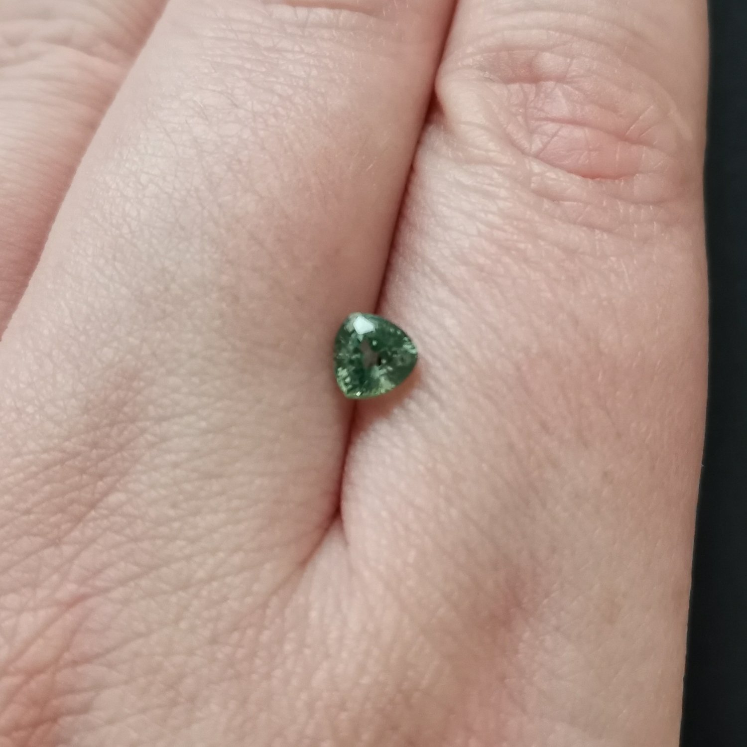 The green sapphire gemstone resting on a hand to give an idea of the gemstones size and colour.