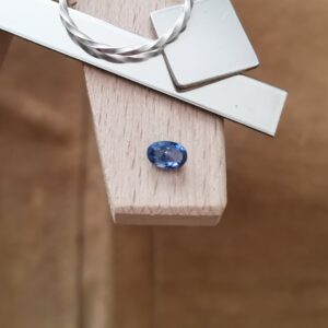 The red blue sapphire oval displayed on a jewellers bench peg with some sterling silver sheet and wire.