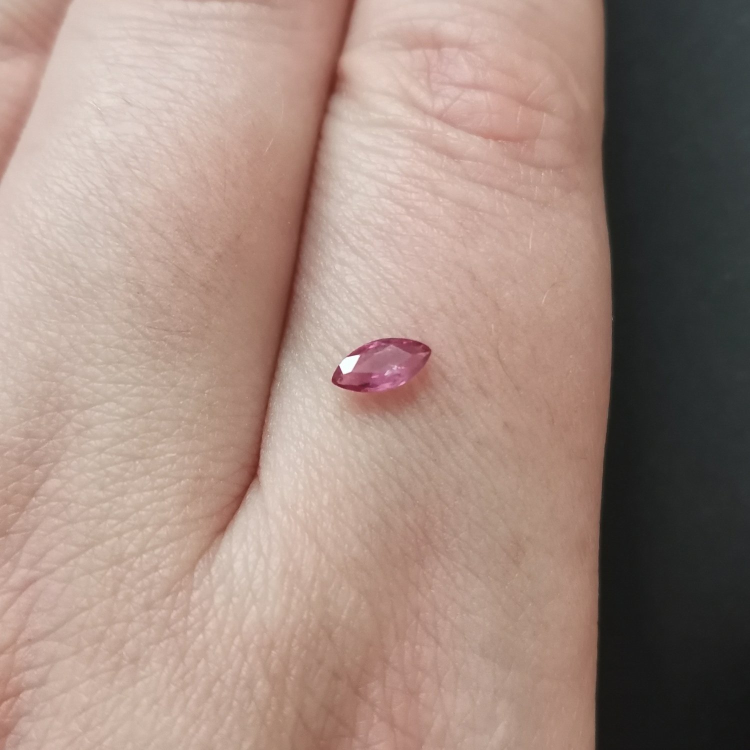 The pinkish red ruby gemstone resting on a hand to give an idea of the gemstones size and colour.