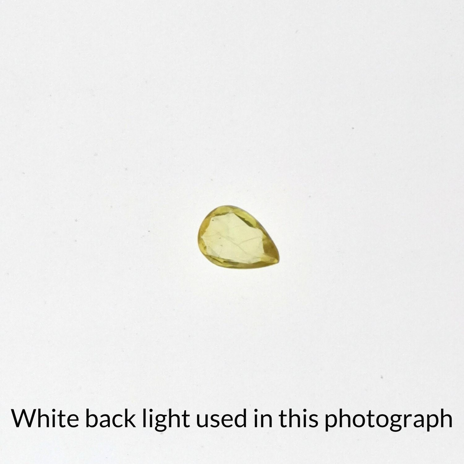 The yellow sapphire teardrop gem is being back-lit with a bright white light to show any inclusions within the gem more clearly.