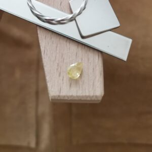 The yellow sapphire teardrop displayed on a jewellers bench peg with some sterling silver sheet and wire.