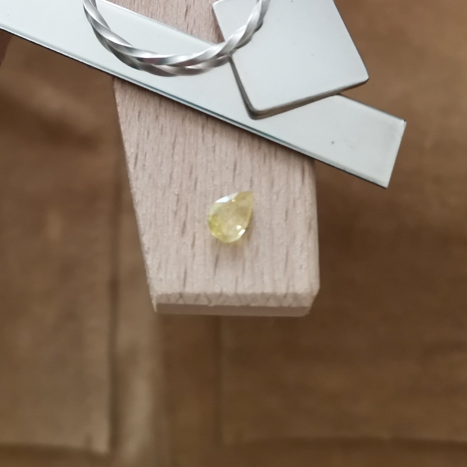 The yellow sapphire teardrop displayed on a jewellers bench peg with some sterling silver sheet and wire.