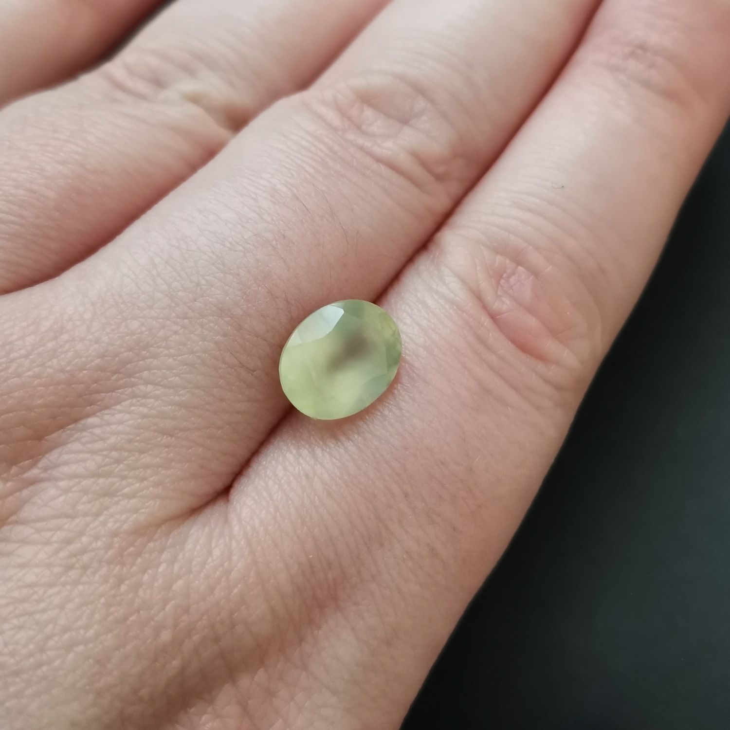 The faceted oval prehnite resting on a hand to show size and colour.