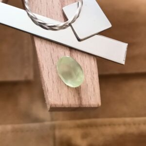 The yellow-green prehnite oval displayed on a jewellers bench peg with some sterling silver sheet and wire.