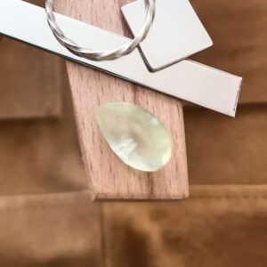 The yellow-green prehnite teardrop displayed on a jewellers bench peg with some sterling silver sheet and wire.